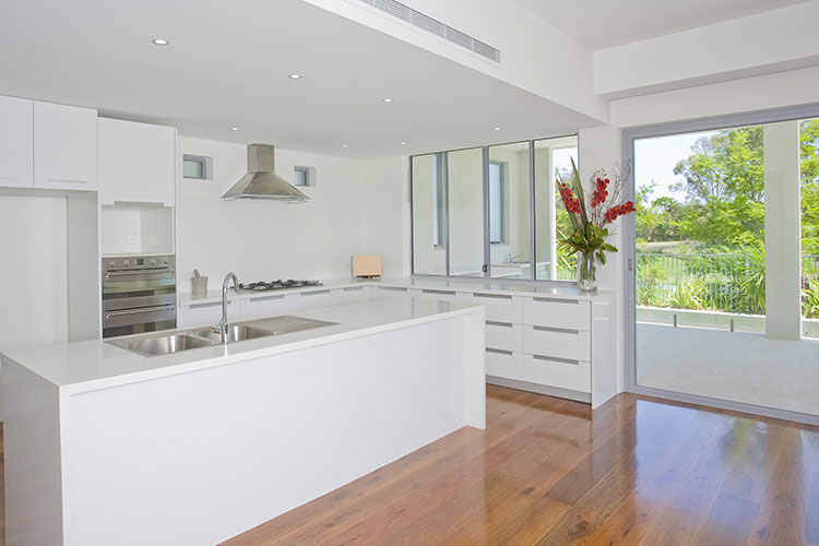 project-10 Cocina moderna blanca con isla central, suelo de madera, encimeras de cuarzo y vistas al jardín exterior