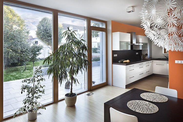 project-11 Cocina moderna con gabinetes blancos, pared naranja, plantas naturales y ventanales panorámicos con vistas al jardín