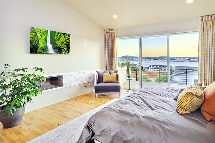 project-12 Dormitorio moderno con chimenea lineal, vista panorámica al lago, suelos de madera y decoración minimalista en tonos grises