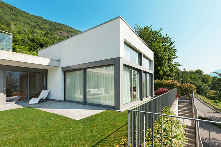 project-7 Villa moderna de dos plantas con fachada blanca, grandes ventanales grises y jardín verde, rodeada de montañas boscosas