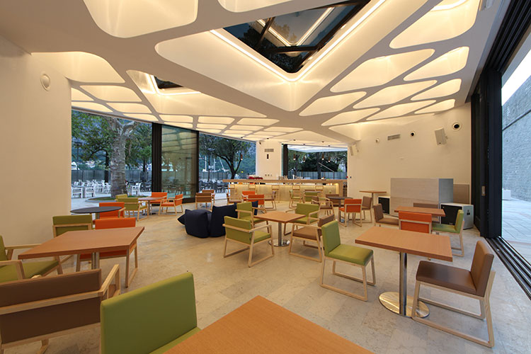 project-9 Cafetería moderna con sillas verdes y naranjas, techo decorativo blanco con iluminación LED y grandes ventanales al jardín